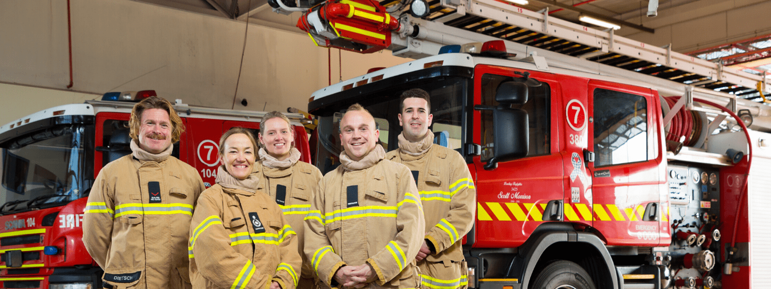A group of five firefighters in front of a truck